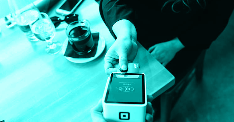 teal monotone photo of a person inserting a card into a handheld vendor payment device to represent credit card fraud.